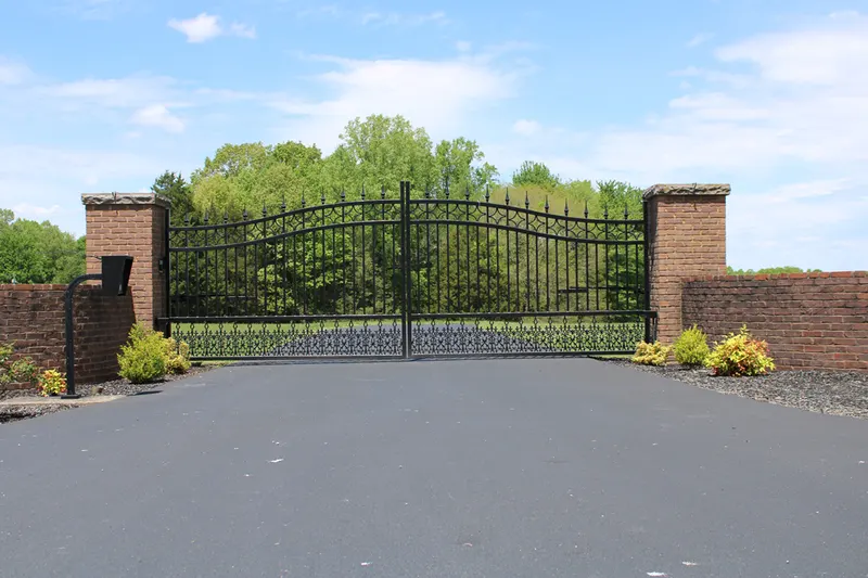 Arched black wrought-iron driveway gate between brick columns