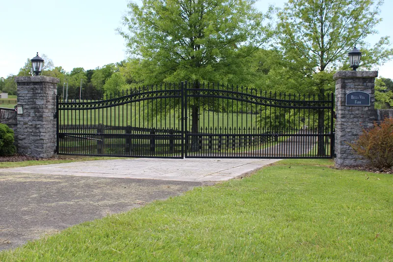 Arched black wrought-iron driveway gate between stone columns
