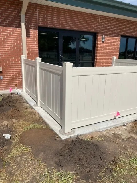 Tan vinyl privacy fence at the back of a brick commercial building